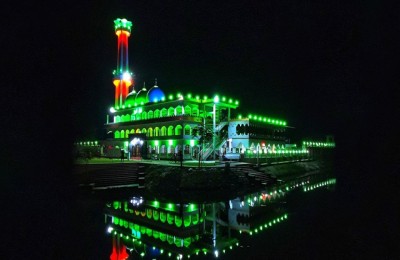 The mosque illuminated with striking green lights, beautifully reflected in water at night.